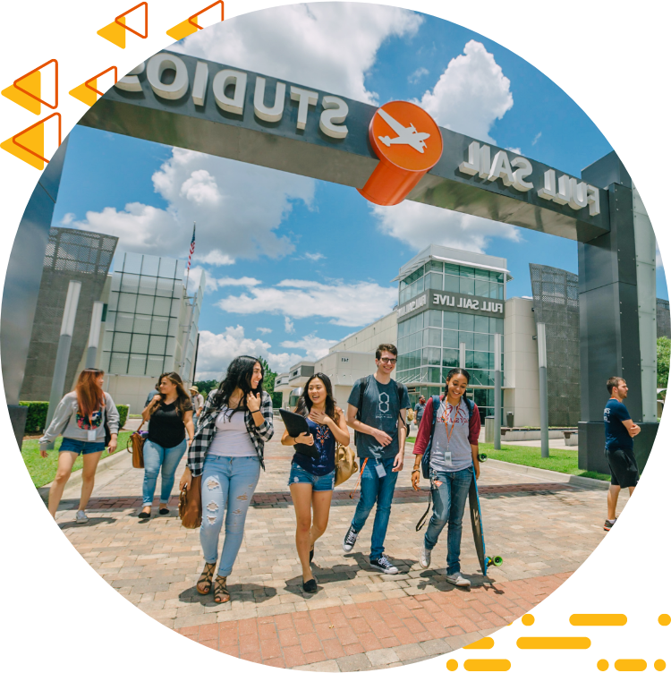 Four students casually chatting and walking under 的 Full Sail Studios archway, a blue sky with clouds in 的 background.